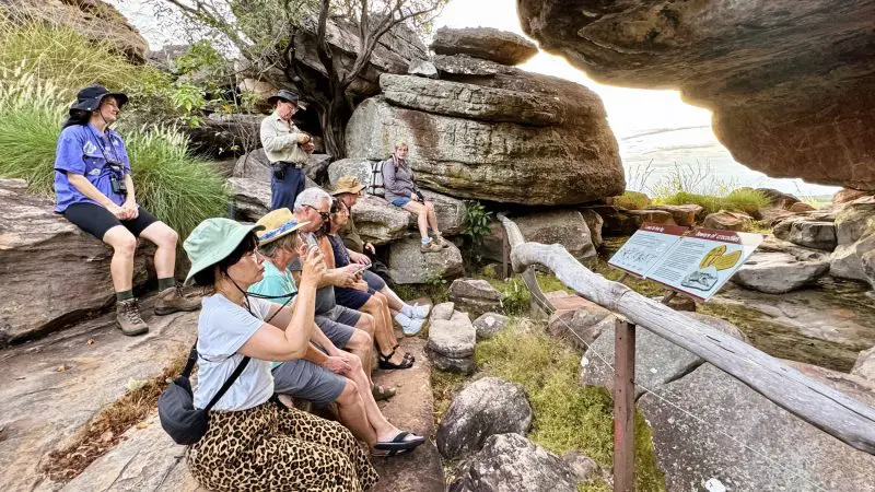 Tour group experiences 1 Day Kakadu Wilderness Escape with Crocodile Cruise, led by guide near rocky outcrops and informative signposting.
