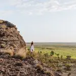 Traveller in white standing atop a rugged cliff, overlooking lush green plains—ideal for an unforgettable 1 Day Kakadu Wilderness tour.