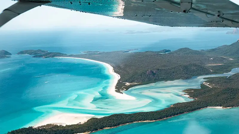 Stunning aerial view of Whitehaven Beach’s turquoise waters and white sands under an aeroplane wing, ideal for tandem skydiving adventure.