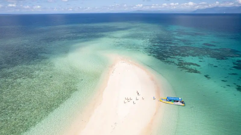 Discover a picturesque sandbank at Great Barrier Reef Eco Adventure, surrounded by crystal-clear blue waters, visitors, and a tour boat.