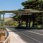 Iconic Great Ocean Road wooden archway sign, framed by lush trees and vivid blue sky during a top-rated 1 Day Rainforest Tour.