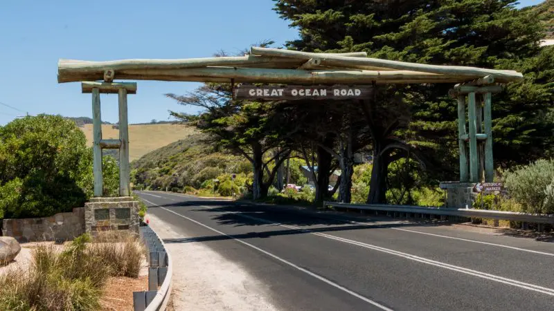 Iconic Great Ocean Road wooden archway sign, framed by lush trees and vivid blue sky during a top-rated 1 Day Rainforest Tour.