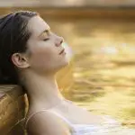 Woman in a white swimming costume relaxing at Peninsula Hot Springs pool during 1 Day Spa Entry Shuttle Bus tour, serene wellbeing experience.