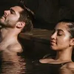 Couple relaxing in a sunlit Peninsula Hot Springs pool, savouring their 1 Day Spa Entry with Shuttle Bus for the ultimate wellness escape.