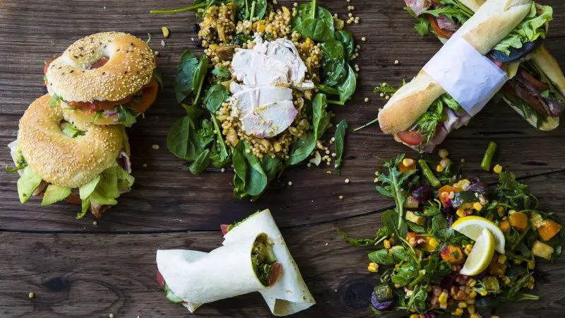 A tempting spread of gourmet sandwiches, fresh wraps, and vibrant salads on a rustic table—ideal prelude to your Peninsula Hot Springs Spa Entry Shuttle Bus experience.