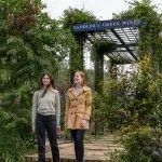 Two women walk beneath a lush vine-clad pergola at Saddler’s Creek Wines during a scenic 1 Day Hunter Valley wine tasting tour.
