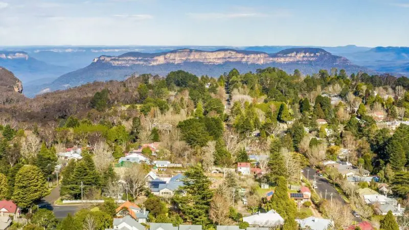 Stunning aerial view of a charming Blue Mountains town, ideal for sunset wilderness tours, beneath a vibrant clear blue sky.