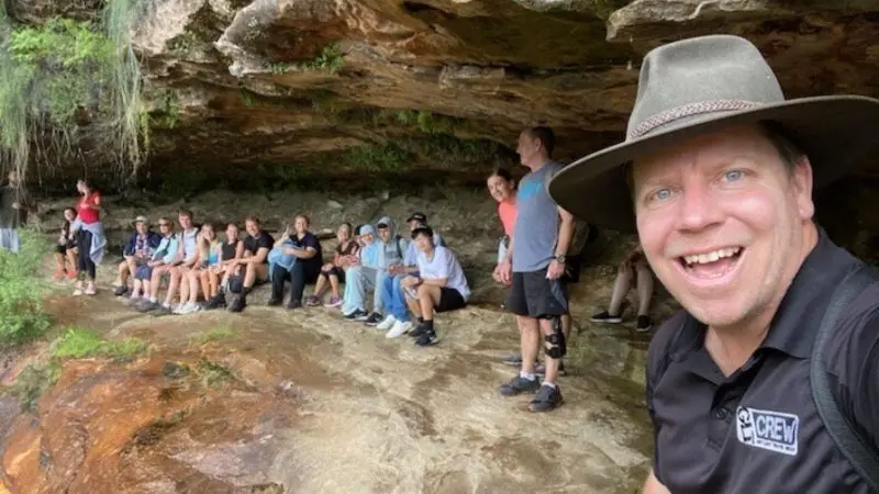 A cheerful man in a hat snaps a selfie with friends amid scenic landscapes on a 1 Day Blue Mountains Sunset Wilderness Tour outdoors.