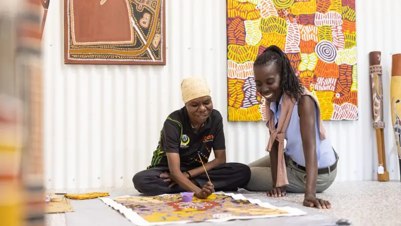 Smiling women create colourful Aboriginal art amid vibrant paintings—an ideal cultural experience before your 1 Day Katherine Gorge Cruise.