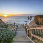 Wooden stairs descend to a golden beach at sunset on the 1 Day Great Ocean Road Sunset Tour from Melbourne, cliffs and sea view.