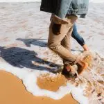 Experience two travellers with rolled-up trousers walking barefoot on the sand during a Great Ocean Road sunset tour from Melbourne.