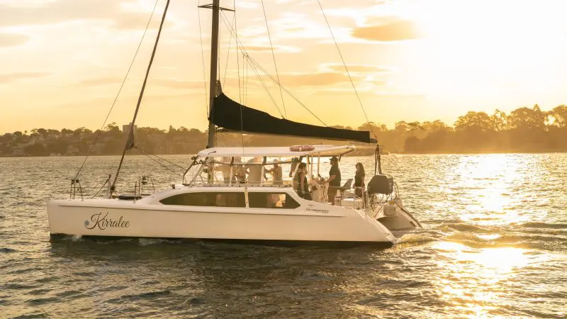 A white catamaran glides at sunset on Sydney Harbour as guests enjoy a BYO Sparkle Cruise, with iconic city views in the background.