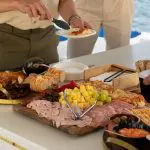 Guests savour a gourmet charcuterie board aboard a Sydney Harbour BYO Sunset Sparkle Catamaran Cruise with stunning waterfront views.