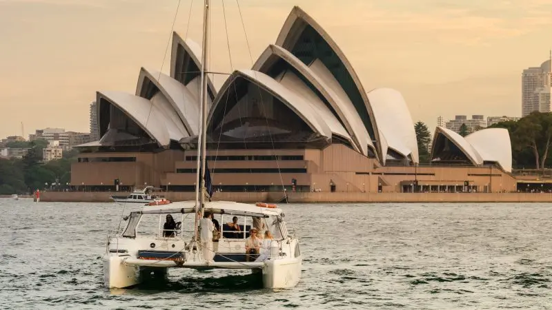 Experience a stunning BYO Sunset Sparkle Cruise on Sydney Harbour, with a catamaran sailing past the iconic Opera House at golden hour.