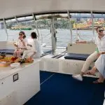Group of friends enjoy food and drinks, laughing together on a Sydney Harbour BYO Sunset Sparkle Catamaran Cruise at dusk.