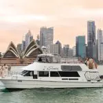 White boat with passengers cruises Sydney Harbour at sunset, golden skies behind Opera House and skyline for iconic Australian views.