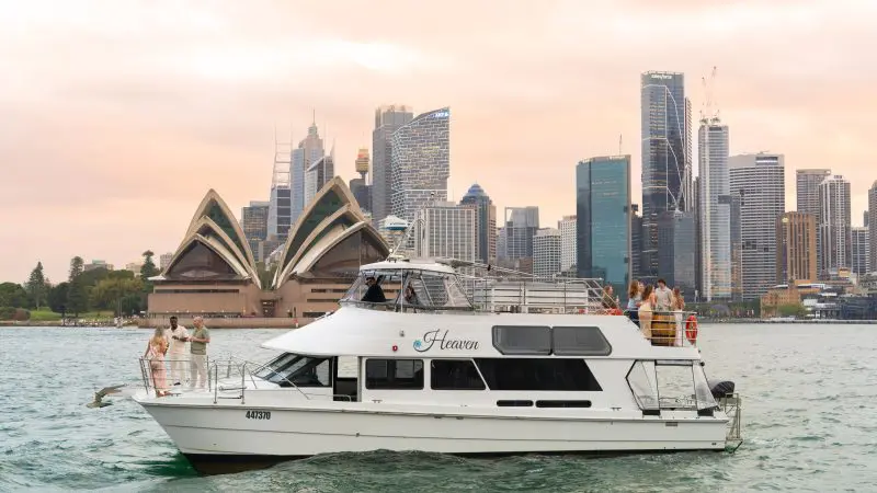 White boat with passengers cruises Sydney Harbour at sunset, golden skies behind Opera House and skyline for iconic Australian views.