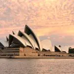 Iconic Sydney Opera House silhouetted at sunset with vibrant pink clouds, viewed on a Sydney Harbour Golden Glow Sunset Cruise.
