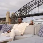 Man relaxing on a luxury yacht with striped cushions, smiling during a Sydney Harbour sunset cruise with iconic bridge views.