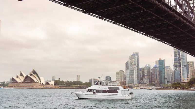 Experience a stunning Sydney Harbour sunset cruise: white boat glides past Opera House & city skyline in golden evening glow.