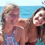 Two young women in swimsuits smiling on a Thundercat 1 Day Whitsunday Islands Adventure with clear blue sea and boat behind them.