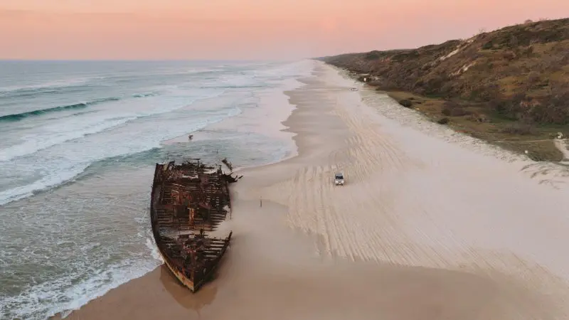 A rusted shipwreck on a long beach with the sun setting in the background