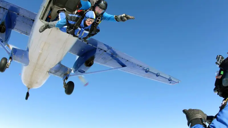 a skydiving instructor and tandem partner jumping out of an airplane with the plane in the background and blue skies