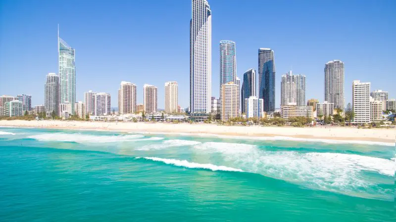 Luxurious high-rise hotels and flats line a pristine sandy beach with turquoise sea waves under a vibrant, cloudless blue sky.