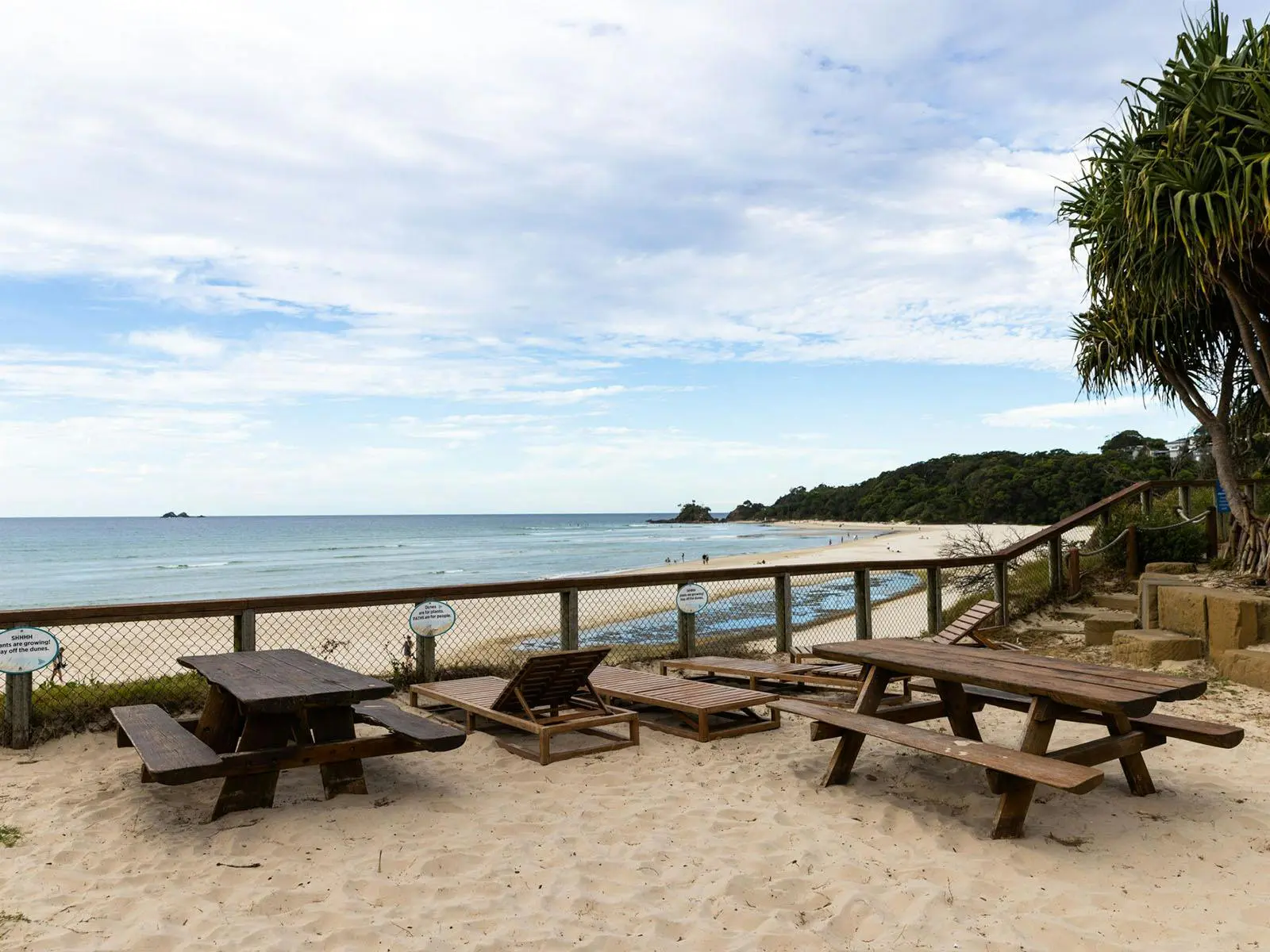 5 wooden beach chairs in the sand along the coast of byron bay