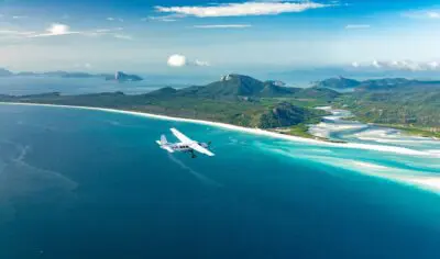 a plane flying over a river delta with a white sand beach