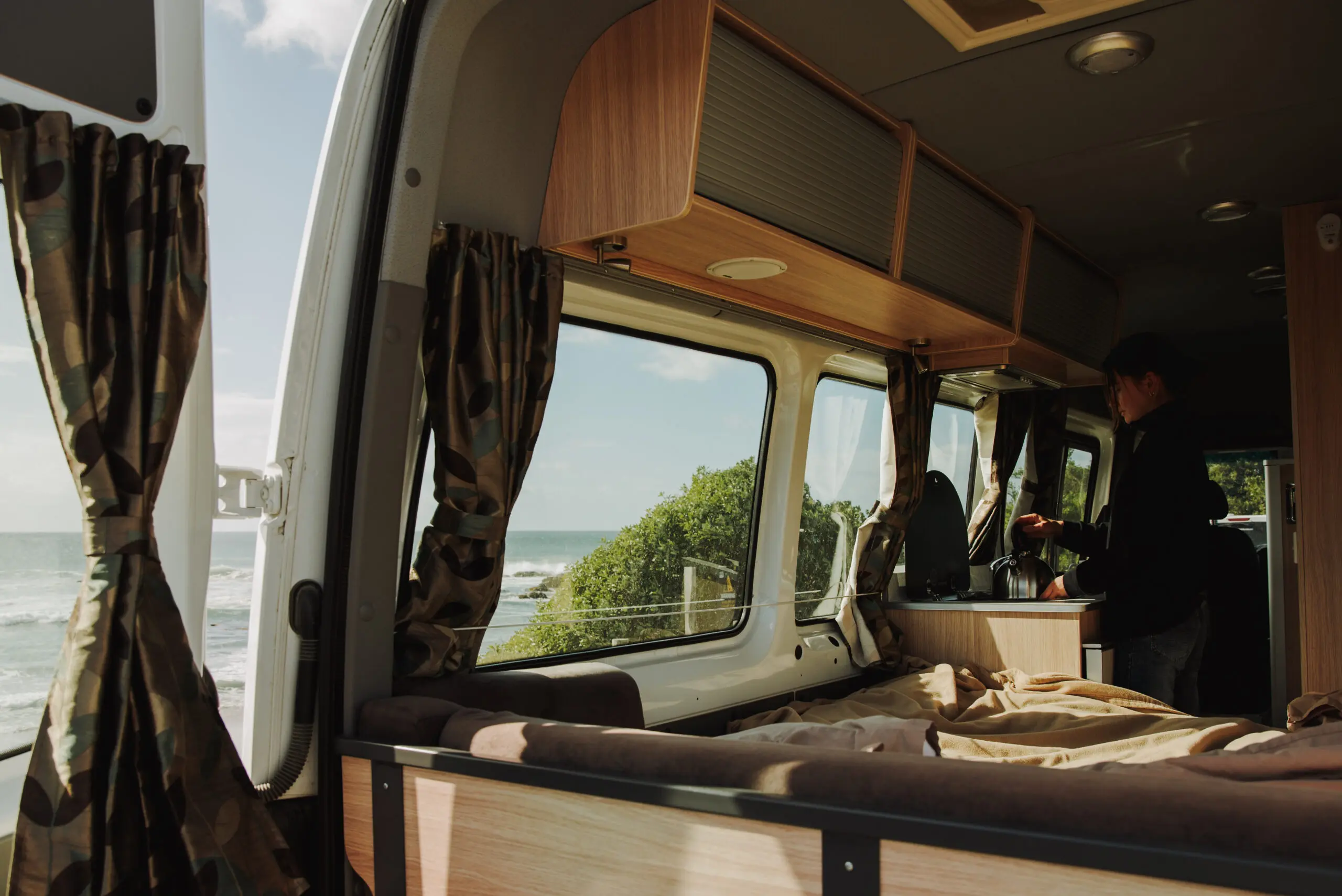 Inside of mIghty campervan looking out the back window to trees and water