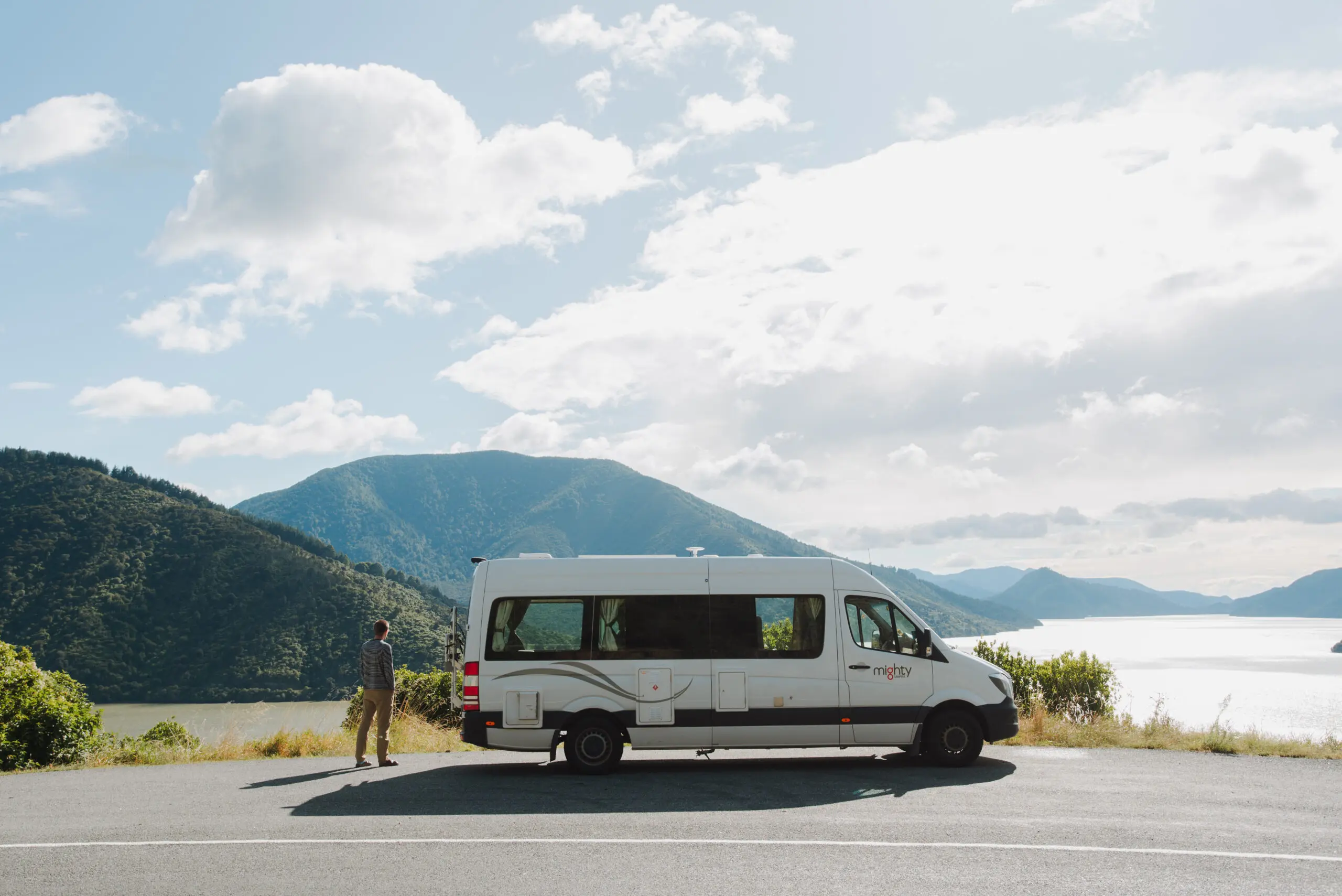Mighty campervan infront of lake and mountains with man next to it