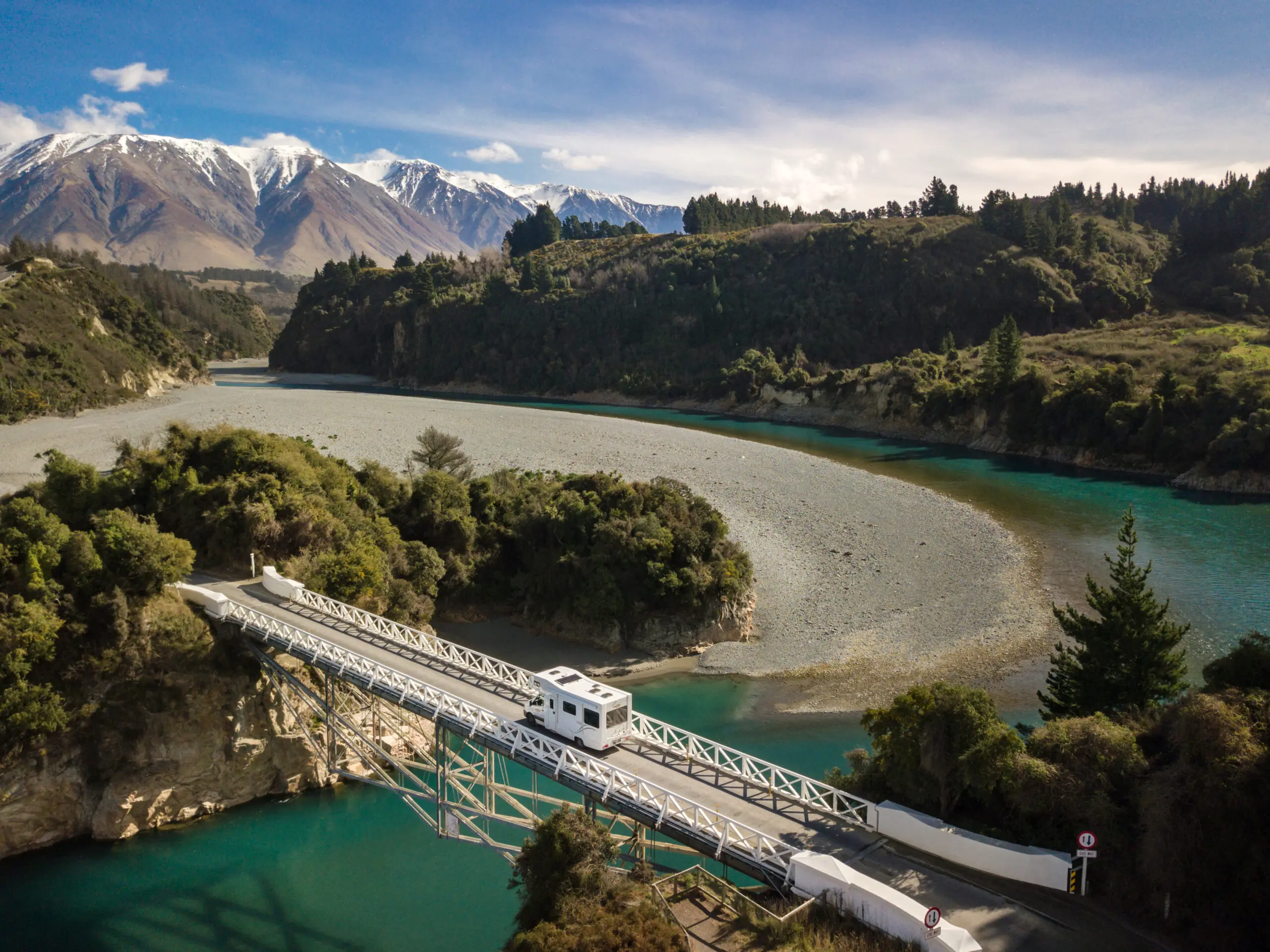 Rv driving on bridge between mountains over a bright blue river