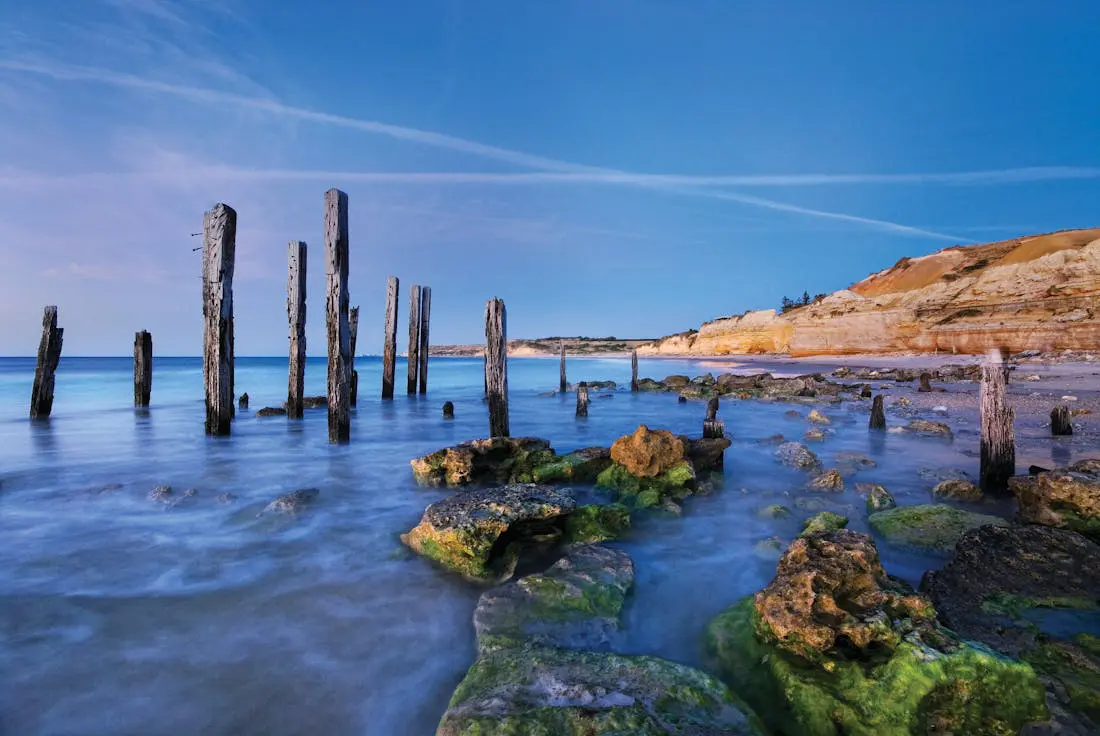 Beautiful sticks in the ocean sticking out of dark blue water with red rock in the background