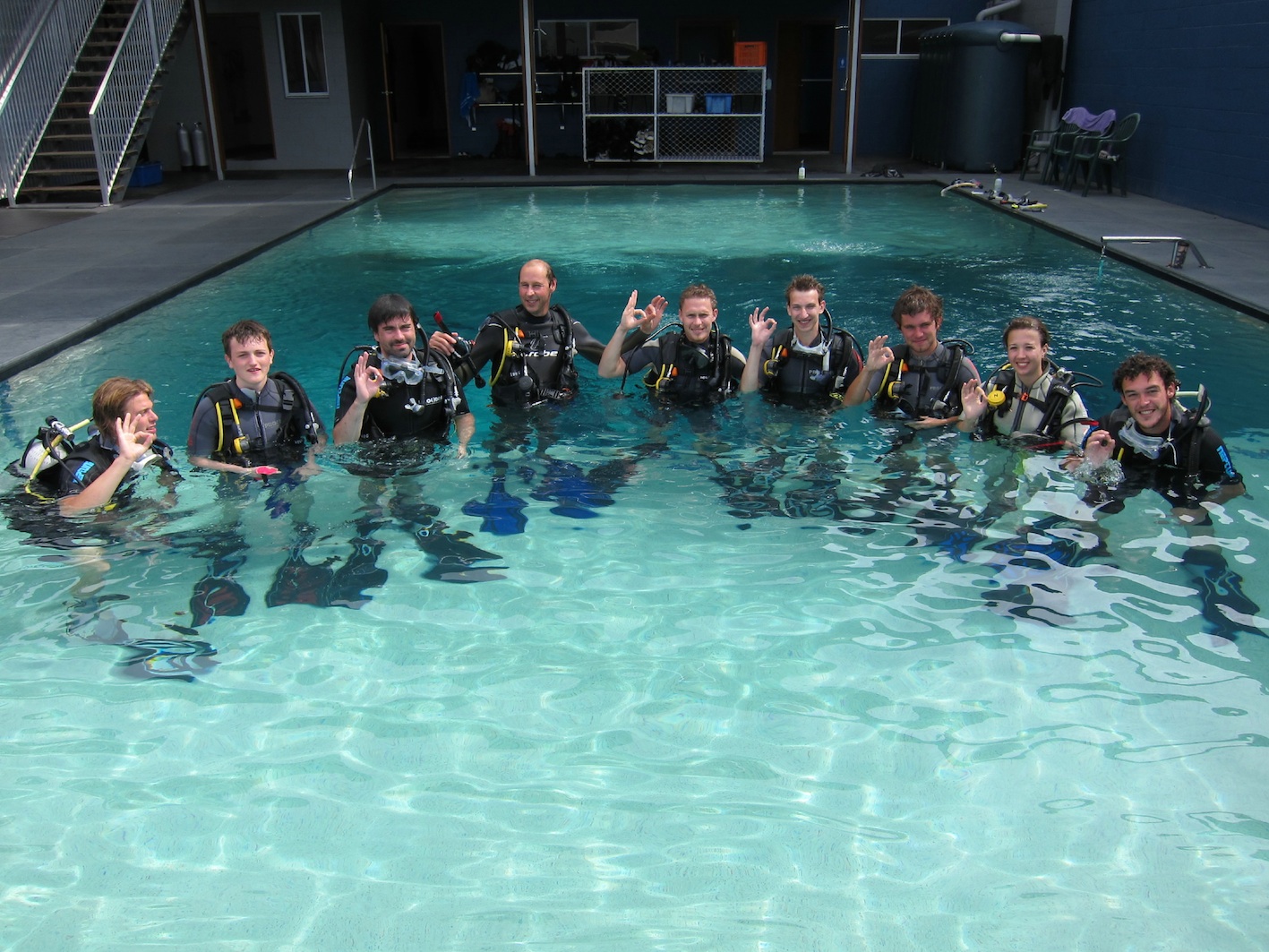Ten scuba divers in full kit smile together in a swimming pool after completing a 3 Day 2 Night Open Water Dive Course for certification.