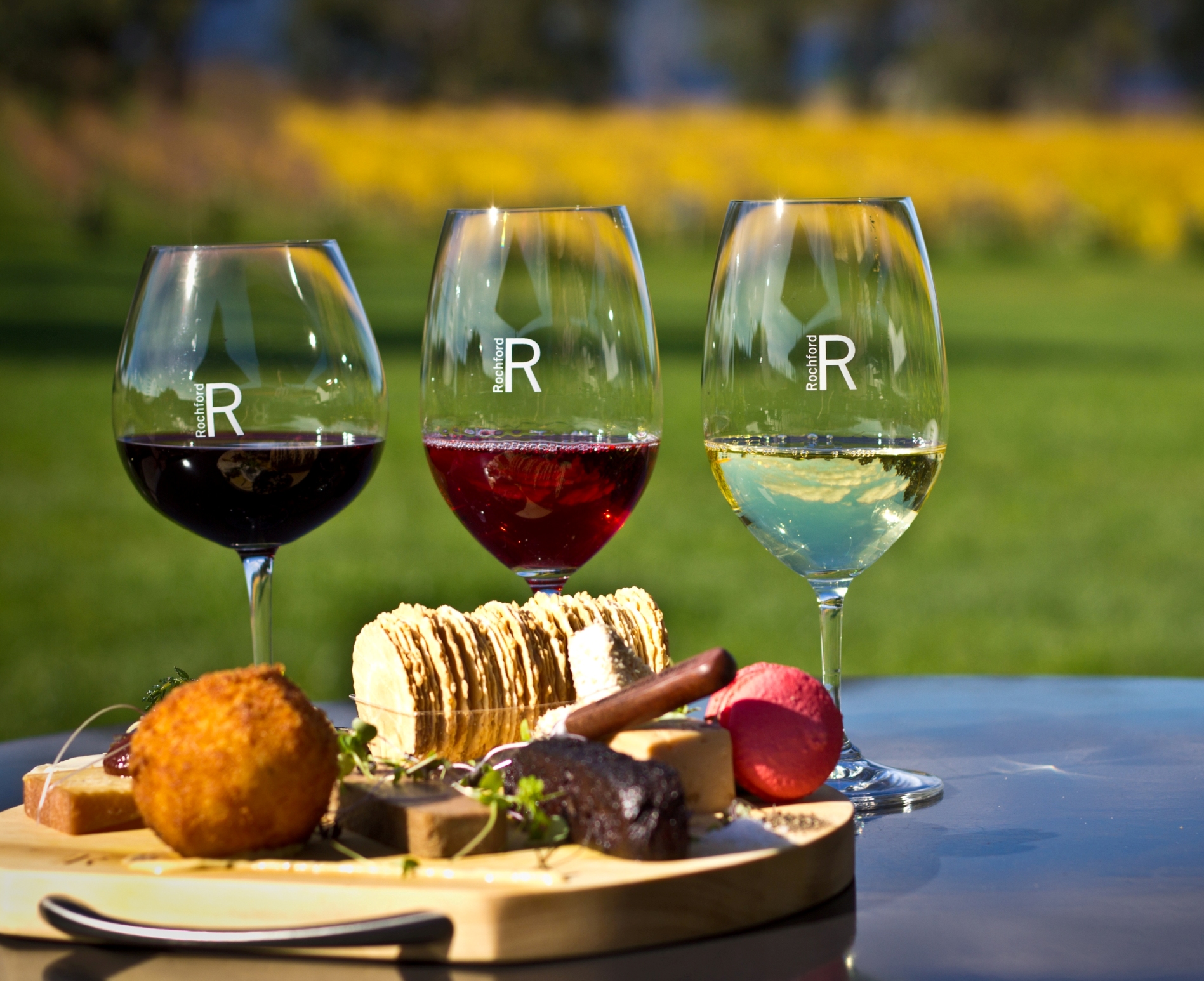 Elegant trio of Yarra Valley wines paired with gourmet appetisers and artisan crackers on a rustic board, ideal for outdoor grazing tours.