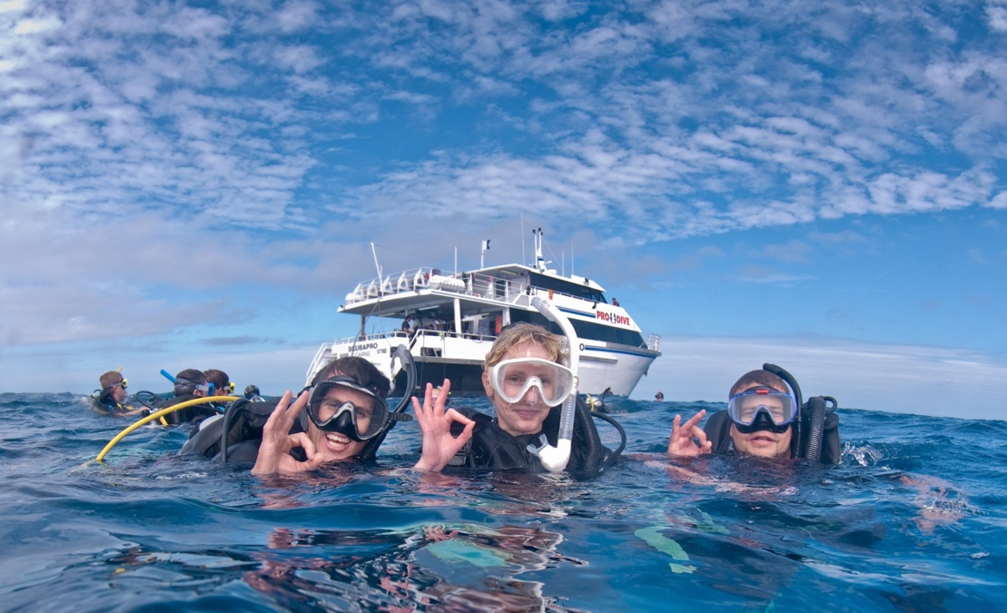 Three scuba divers signal OK underwater near a dive boat during a PADI Rescue Diver Course, demonstrating safe scuba diving skills.