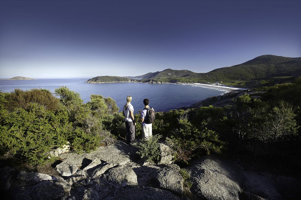 Two people stand on rugged rocks, taking in panoramic views of Wilsons Promontory Bay during a Go West Tours 1 Day guided tour.