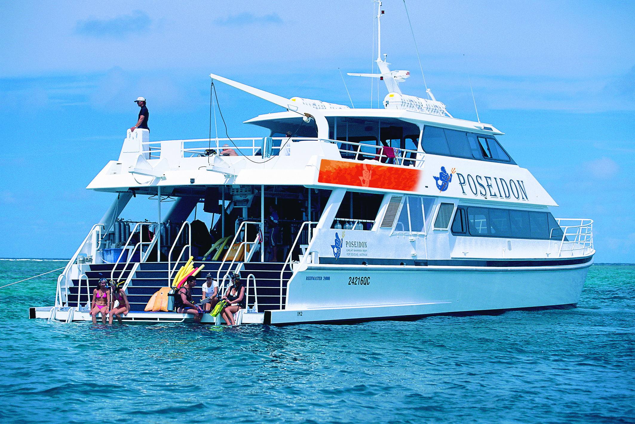 Adventure seekers gear up for a Poseidon Snorkel Dive from a pristine white boat anchored in crystal-clear blue tropical waters.