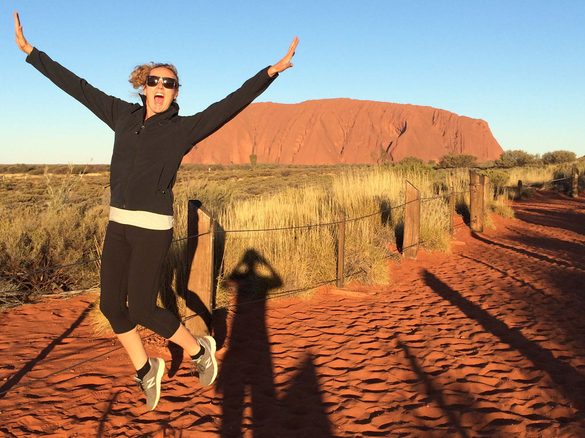 Excited woman jumps on vibrant red dirt track by Uluru, Australia, during a 3-night Rock The Centre Yulara to Yulara tour.