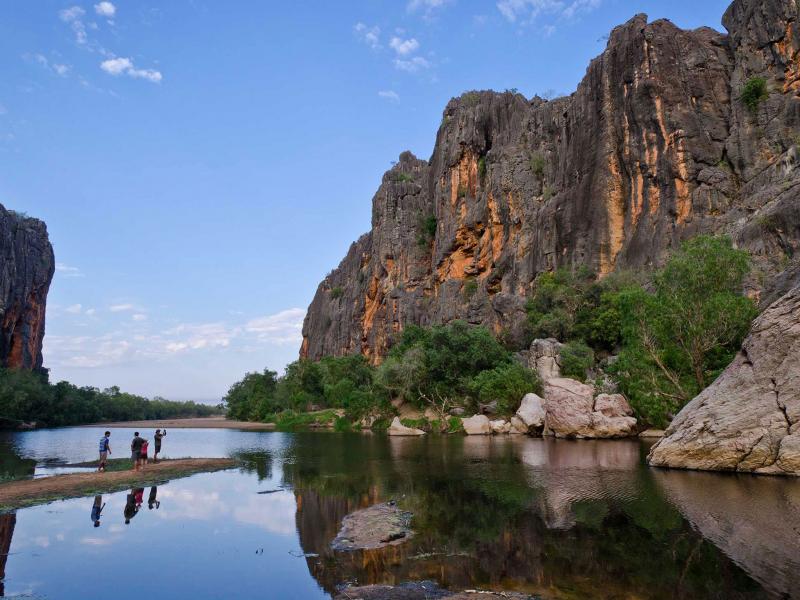 a cliff face beside a river with people on one side