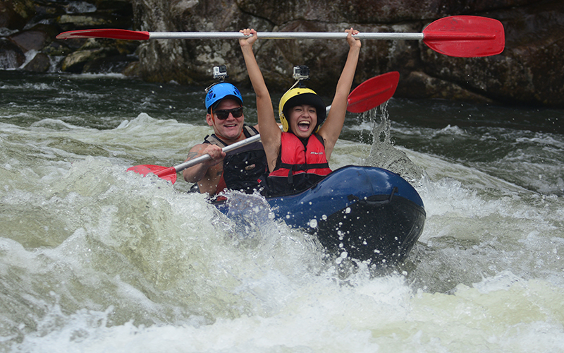 Adventurers in helmets and life jackets conquer rapids at Mission Beach, raising paddles high as water splashes during full-day rafting.