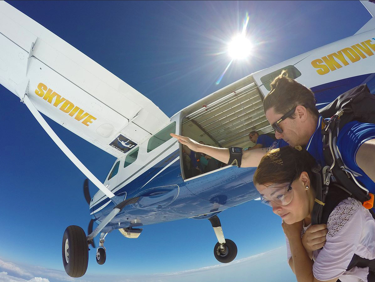 Experience the thrill of a Skydive Sydney tandem jump as two people leap from an aeroplane, surrounded by sunlit skies and scenic clouds.