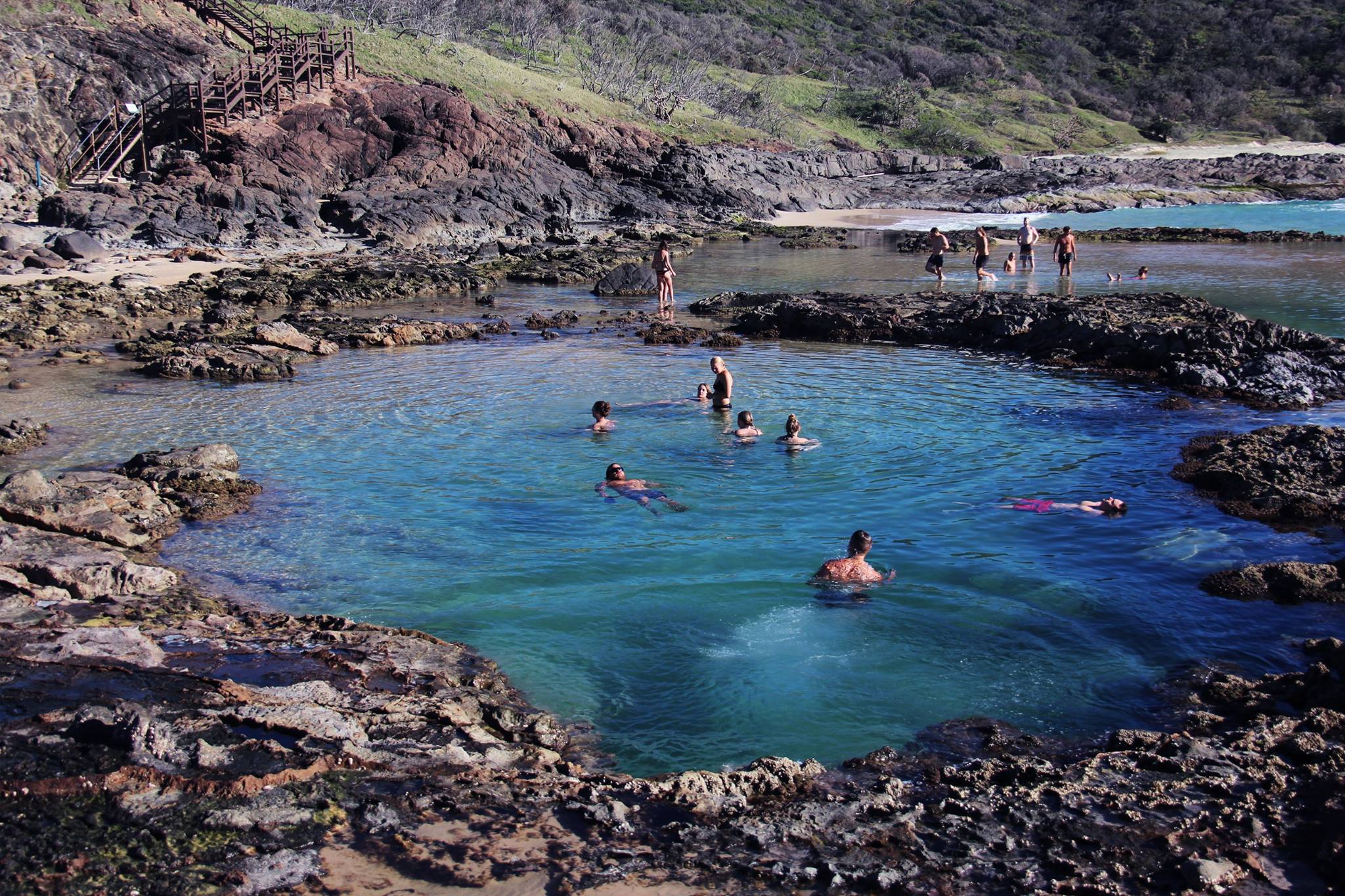 Adventurers swim in a stunning seafront rock pool on a 3 Day K’gari tour with dormitory accommodation at vibrant Rainbow Beach.