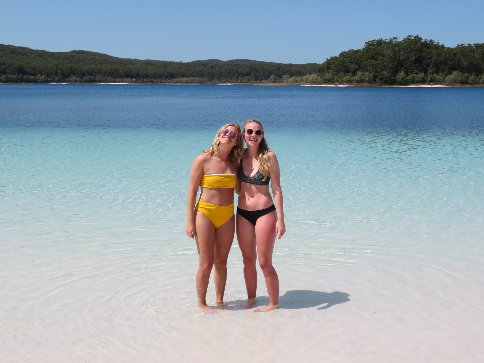 Two women in swimming costumes smile in crystal-clear water during a 3 Day K'gari Adventure with dormitory accommodation at Rainbow Beach.