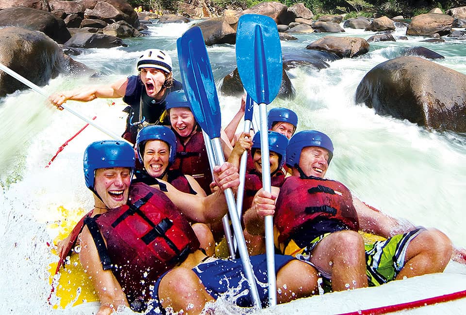 Group of six adventurers paddling and laughing through intense Tully River rapids on a 1 Day White Water Rafting Raging Thunder tour.