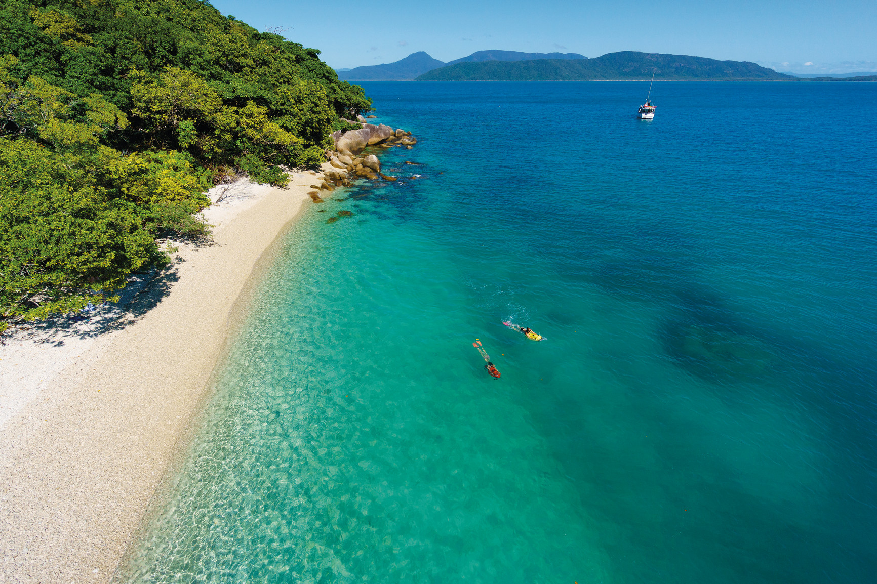 Spectacular aerial view of snorkellers exploring crystal-clear waters off Fitzroy Island’s pristine tropical beach on a half-day tour.