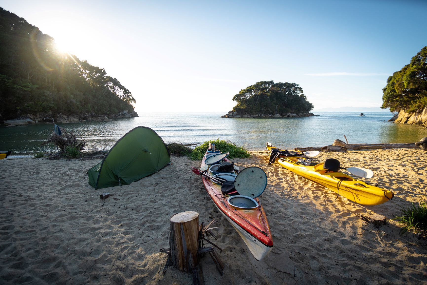 Kayaks and a green tent rest on a pristine sandy beach beside tranquil waters and scenic islands—ideal for a Three Day Classic adventure.