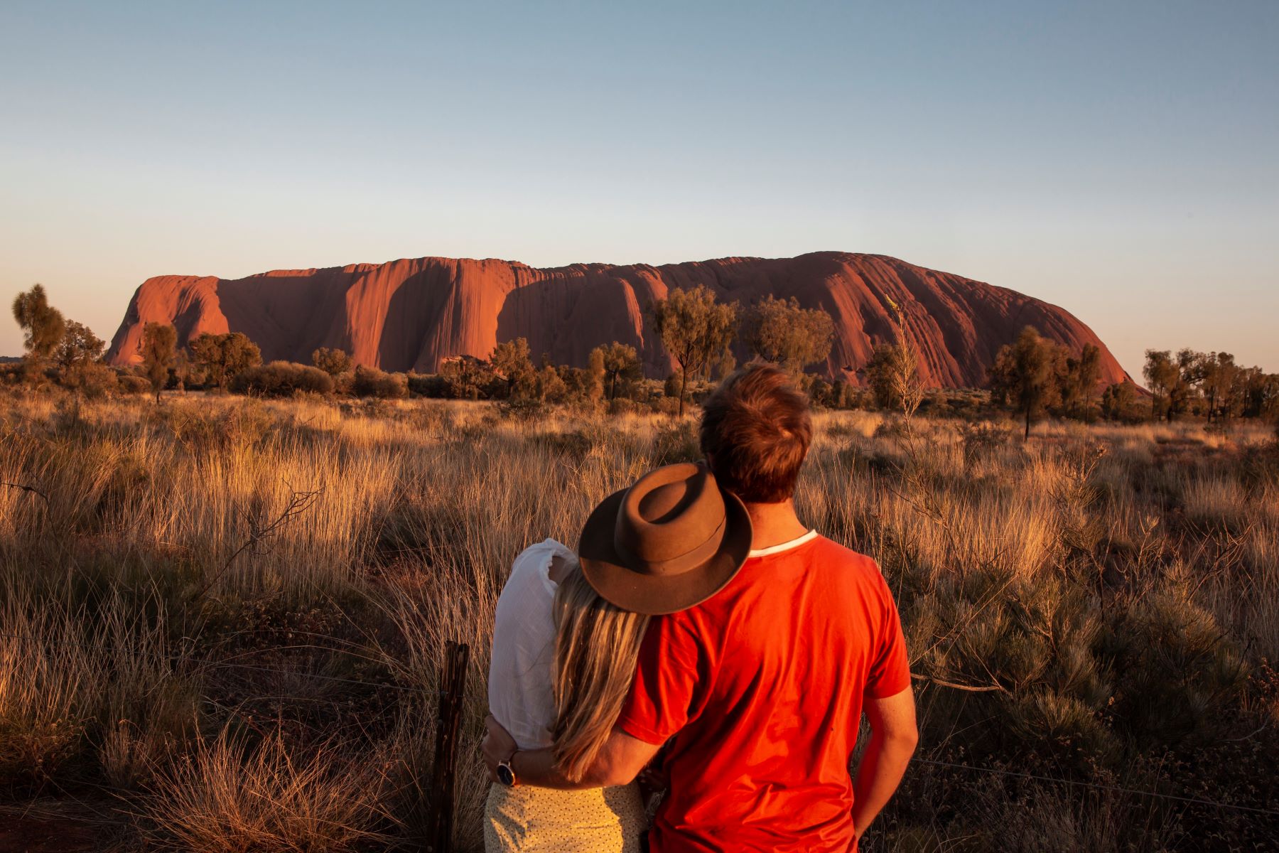 Couple gazes at Uluru during a stunning sunset on a 7-day Adelaide to Uluru Adventure by Untamed Escapes, Australia tour.