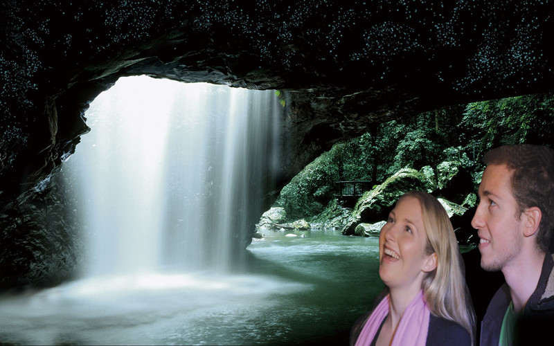 Smiling couple pose by a stunning cave waterfall during a popular Natural Bridge Glow Worm Night Tour from the Gold Coast, Australia.